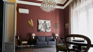 Une pièce avec un sol à carreaux, un canapé gris, une table à manger avec des chaises, un lustre et des éléments de décoration murale.