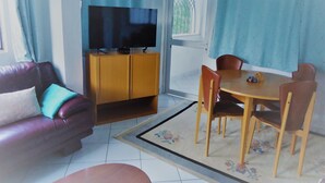 Una sala de estar con un sofá de cuero, un televisor sobre un mueble de madera, una mesa de comedor con sillas y una ventana con cortinas.