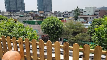 Vista desde un balcón con barandilla de madera, que se extiende sobre un paisaje urbano con diversos edificios, incluido un rascacielos, y algo de vegetación.