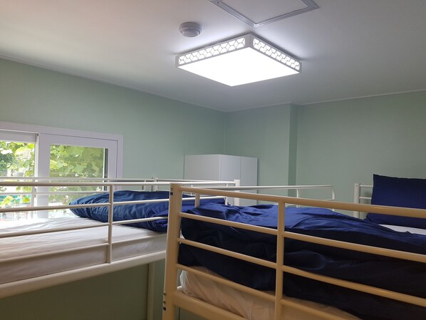 A dormitory room with bunk beds, a window, and a ceiling light fixture.