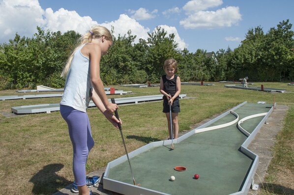 A miniature golf course with a green playing surface, white boundary lines, and a few golf balls and a red ball. - Møgeltønder Camping & Cottages (Tonder)