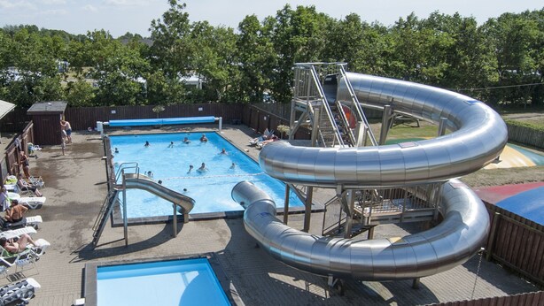 Una piscina con tobogán y sillas de descanso.