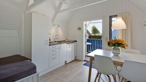 Una cocina moderna con armarios blancos, un comedor con mesa y sillas, y vista al exterior a través de una puerta.