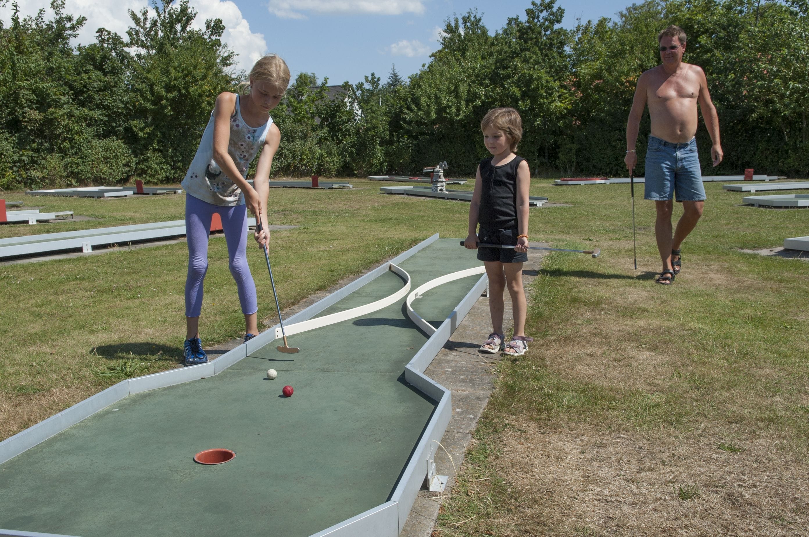 A miniature golf course with a green putting green, a red ball, and a hole.