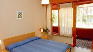 A bedroom with a bed, bedside table, lamp, window with curtains, and a small picture on the wall.
