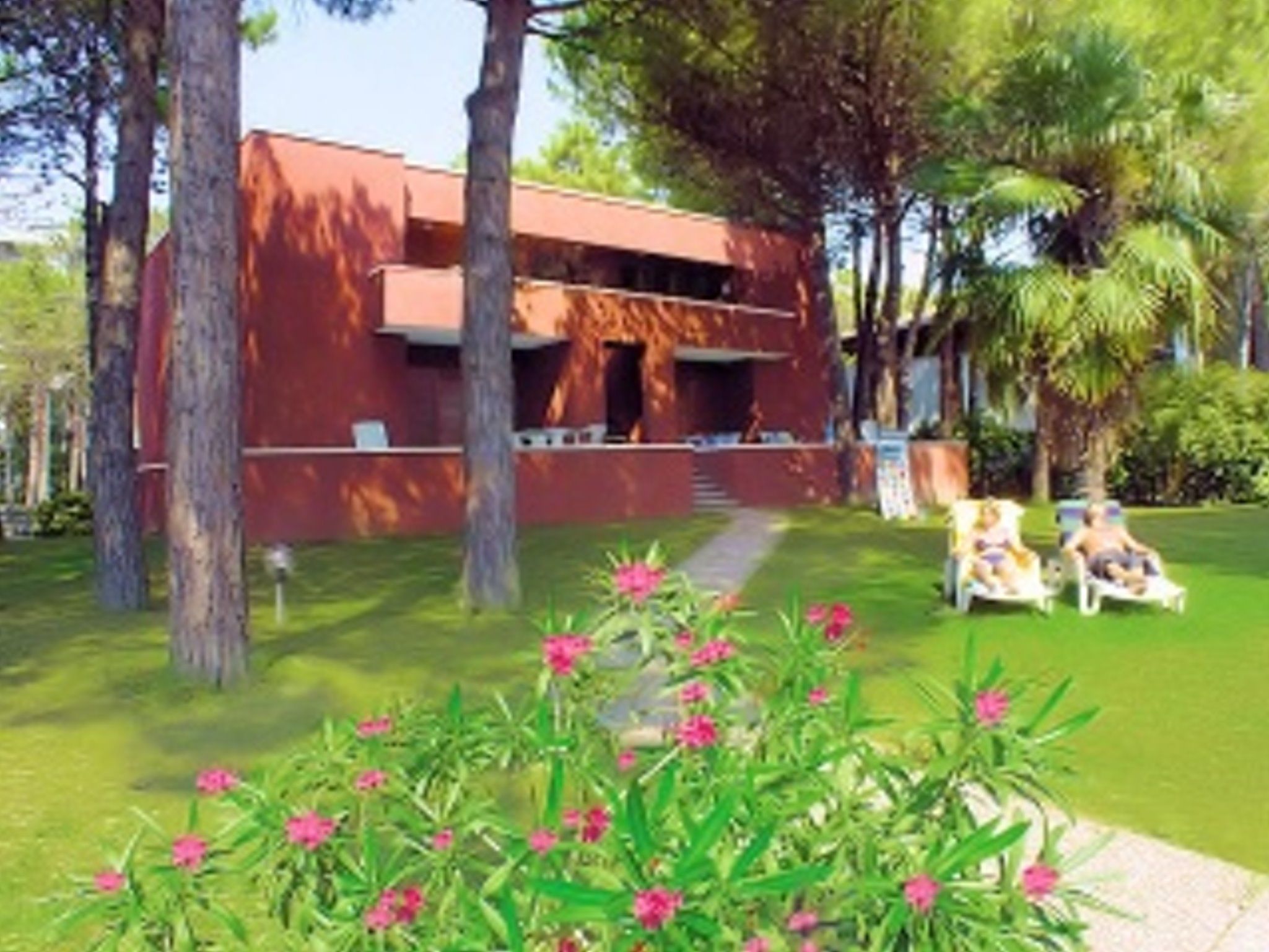 A modern building with a red facade, surrounded by lush greenery and palm trees. There are outdoor seating areas with white chairs.