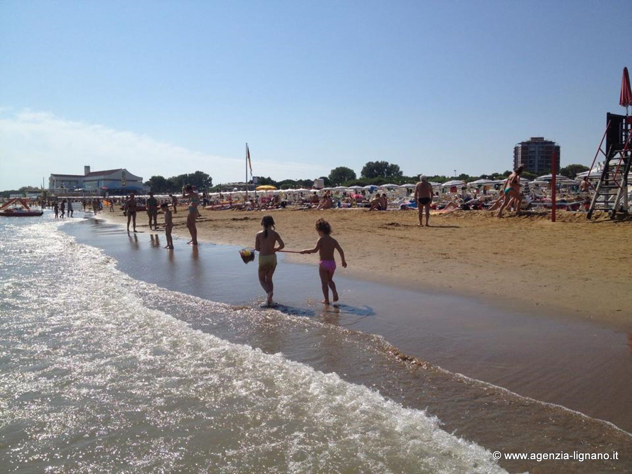 A beach with people walking along the shore, umbrellas, and beach chairs.