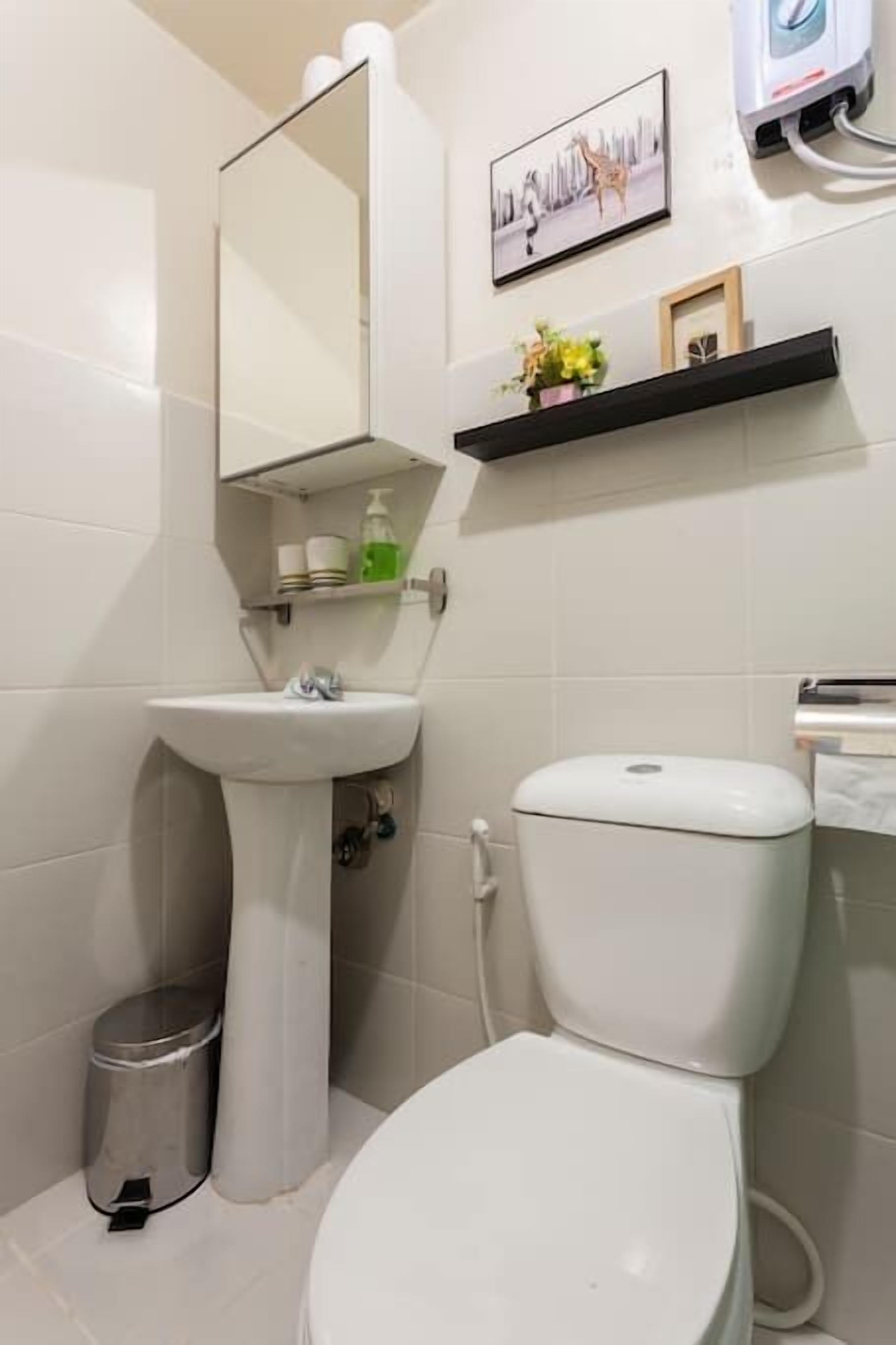 Et badeværelse med et pædebordsvask, toilet og et spejl over vasken. Der er hylder over vasken med toiletartikler og et billede på væggen.