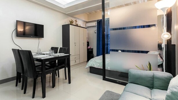 Un dormitorio moderno con cama, televisor montado en la pared, zona de comedor con mesa y sillas, y un pequeño sofá.