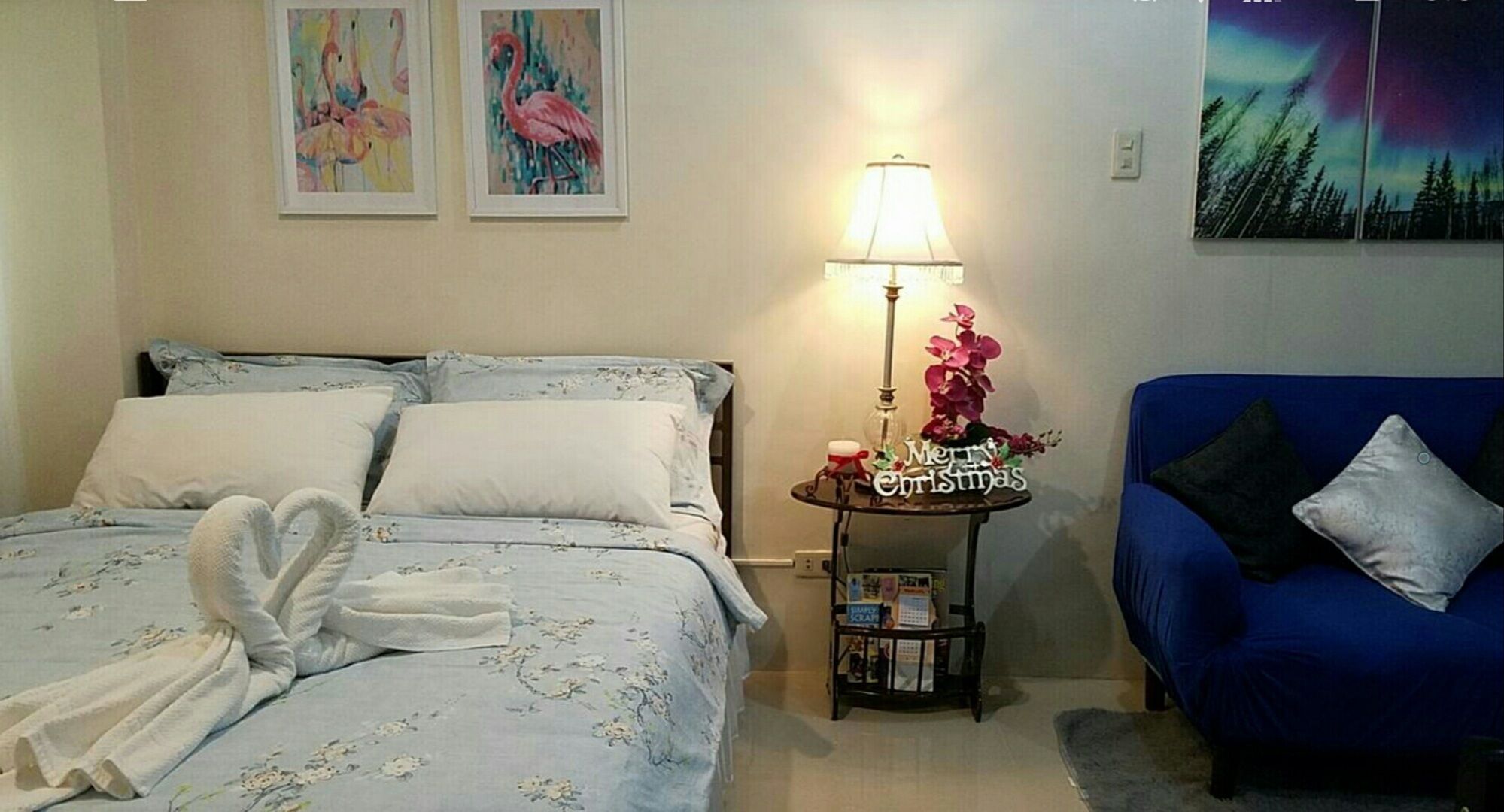 Een slaapkamer met een bed, een blauwe bank, een nachtkastje met een lamp en wanddecoratie.