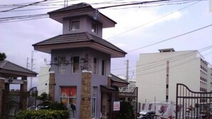 Un edificio de varios pisos con una estructura central tipo torre, rodeado por un área vallada y un pequeño jardín.