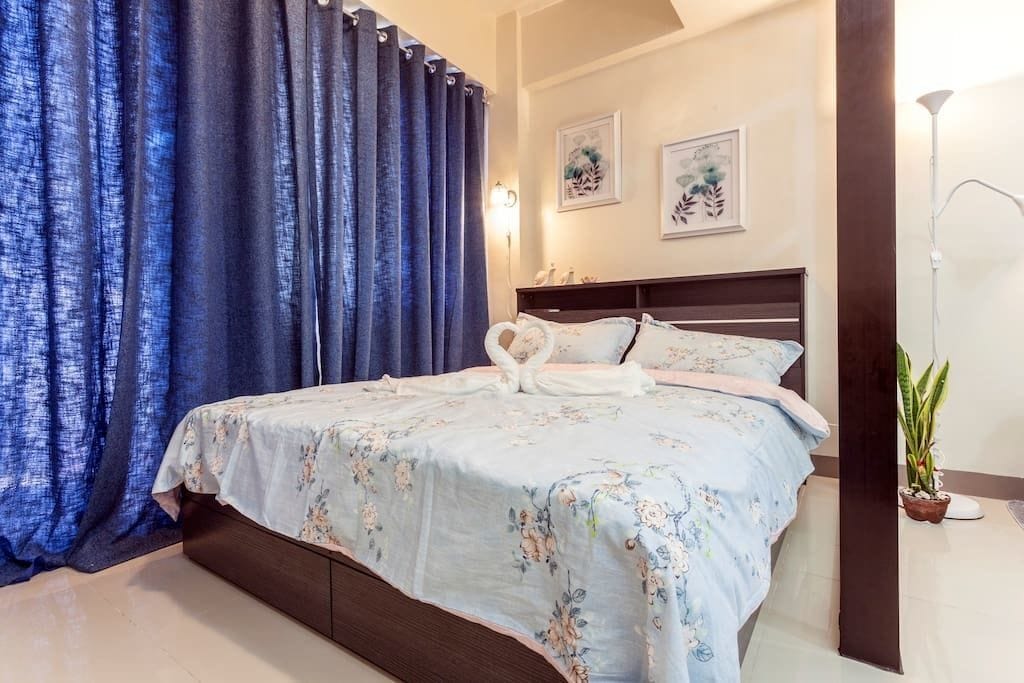 A bedroom with a bed, curtains, a bedside lamp, and a potted plant.