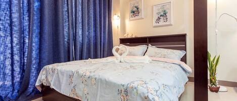 A bedroom with a bed, curtains, a bedside lamp, and a potted plant.