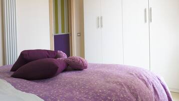 Ein Schlafzimmer mit einem Bett, violetter Bettwäsche, einem Kleiderschrank und einer Tür mit Streifenmuster.