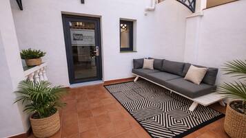 A cozy outdoor seating area with a sofa, potted plants, and a patterned rug.