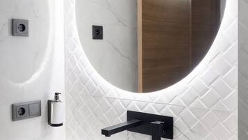 Une salle de bain avec un lavabo en marbre blanc, un miroir rond et une porte en bois.