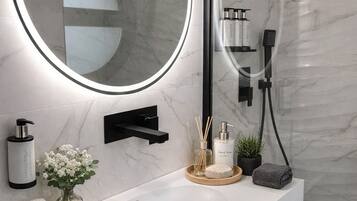 A modern bathroom with a white vanity, a large mirror with a circular frame, and a handheld showerhead.