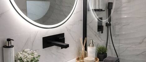 A modern bathroom with a white vanity, a large mirror with a circular frame, and a handheld showerhead.