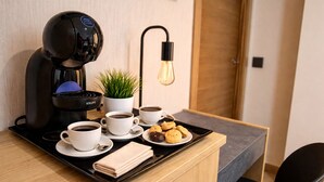 A coffee station with a Krups coffee maker, two cups of coffee, a plate of cookies, a small potted plant, and a wall-mounted light fixture. - NerjaRooms (Nerja)