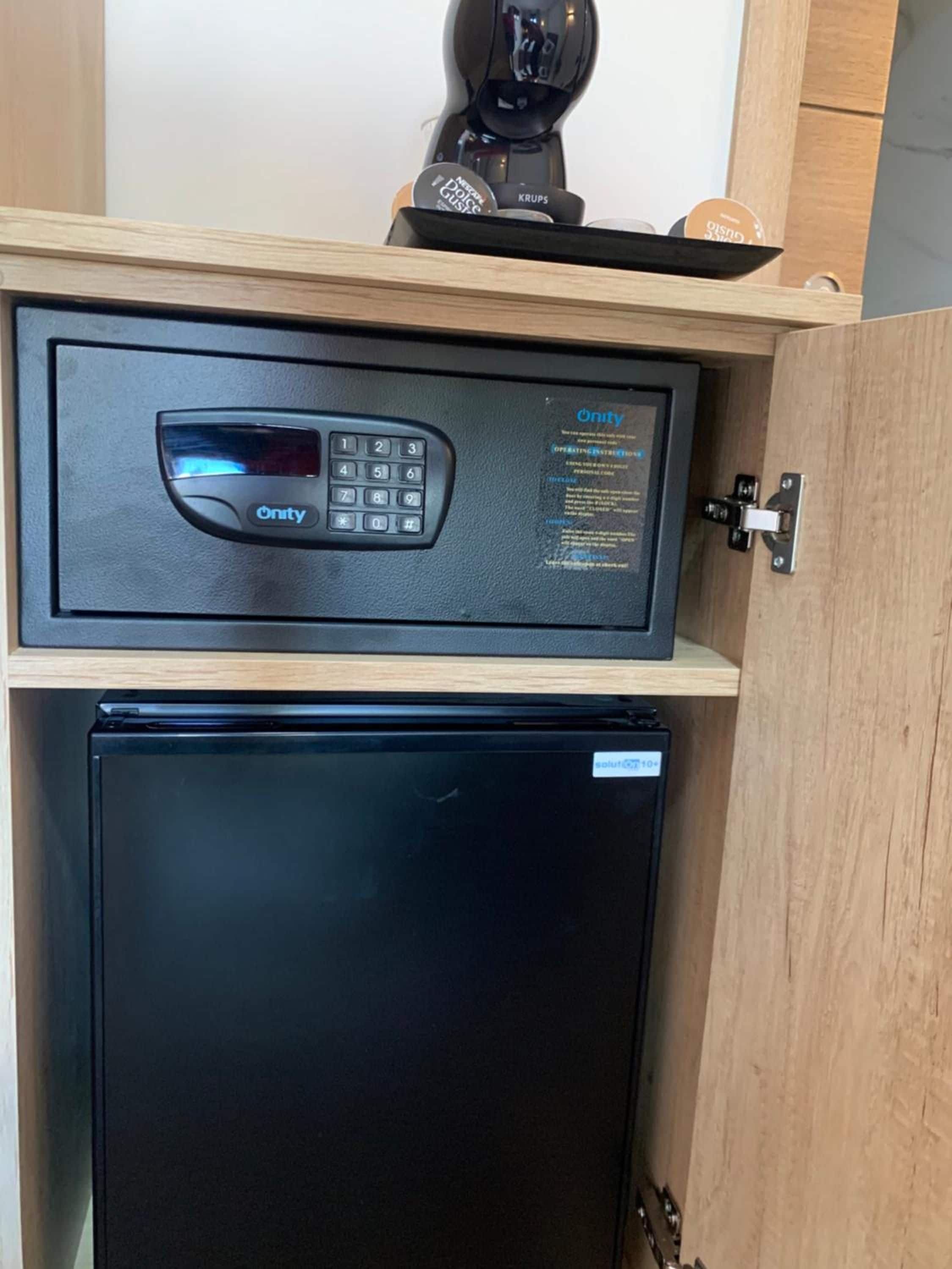 Un refrigerador negro con un panel de control encima, un estante de madera y una cafetera sobre el estante.