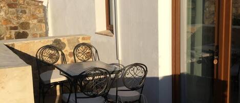 A patio with a table and chairs, a stone wall, and a building with a tiled roof and a sliding glass door.