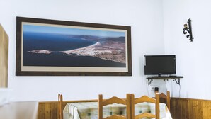 Een eetgedeelte met een tafel gedekt voor twee personen, een ingelijste foto aan de muur en een aan de wand bevestigde televisie.