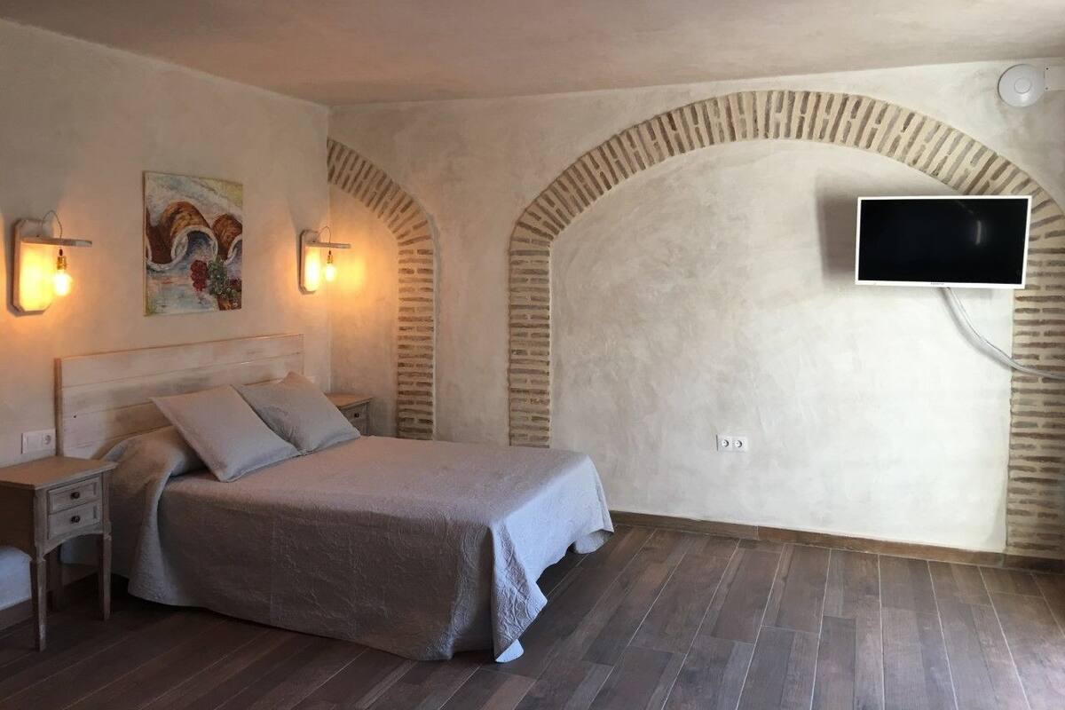 Une chambre à coucher avec un lit, des tables de chevet, un téléviseur fixé au mur et des arches en briques.