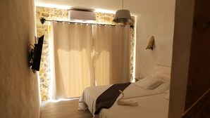 Een slaapkamer met een stenen muur, een bed met een deken, een hanglamp en een raam met gordijnen.