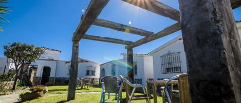 A courtyard with a wooden pergola, outdoor furniture, and a white building with a tiled roof.