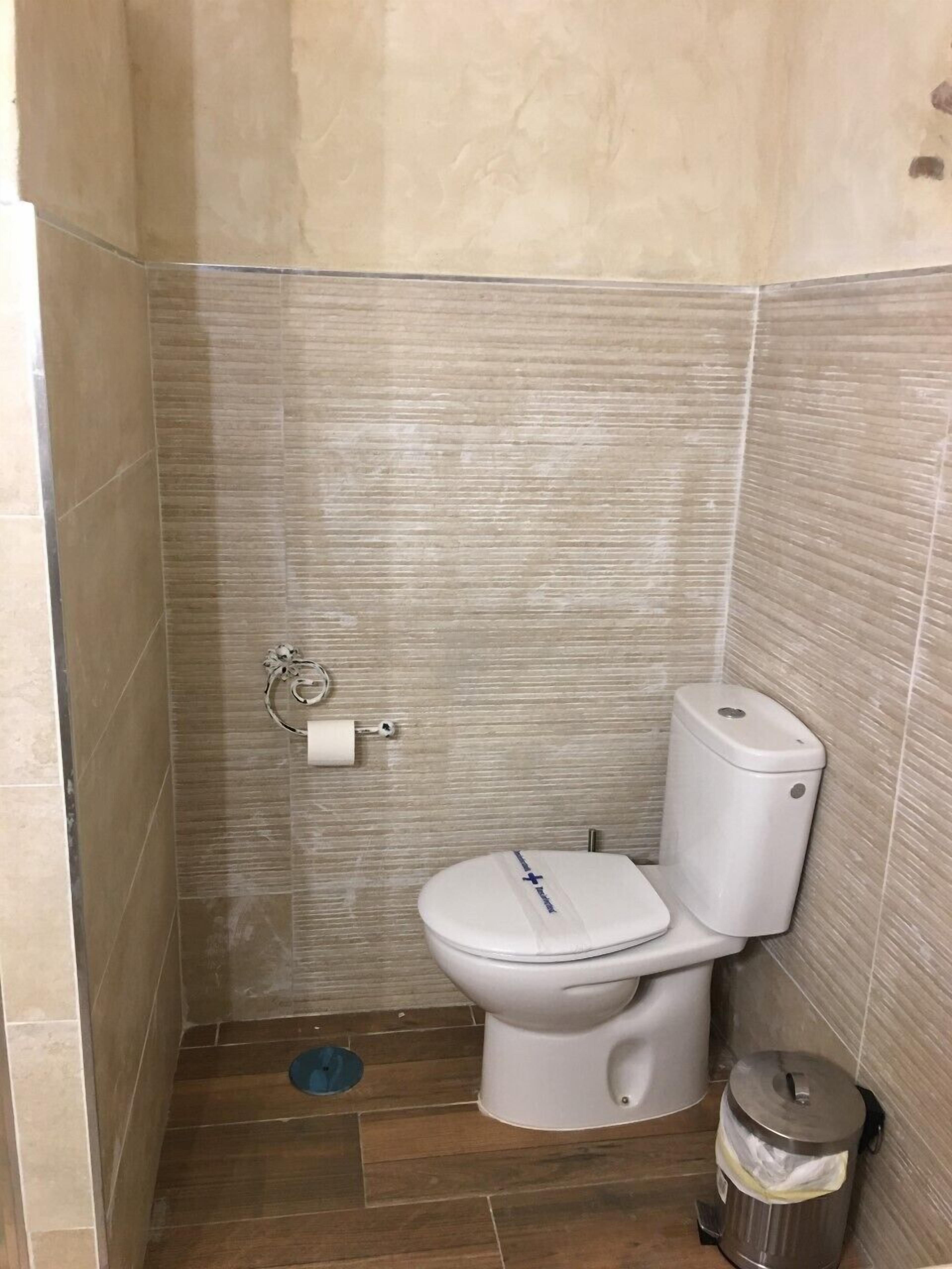 A small bathroom with a toilet, a trash can, and a toilet paper holder on the wall.