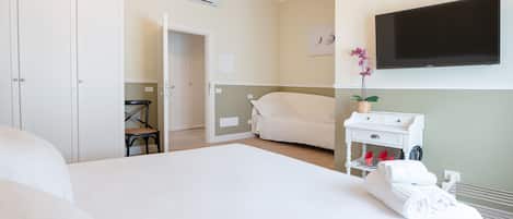 A hotel room with a bed, a chair, a TV, a small table with a plant, and a white wardrobe.