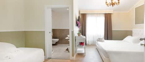 A hotel room with a bed, a bedside table, a mirror, a chandelier, and a bathroom visible through an open door.