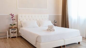 Una cama bien hecha con un edredón blanco, una mesita de noche pequeña con una lámpara y una orquídea en maceta.