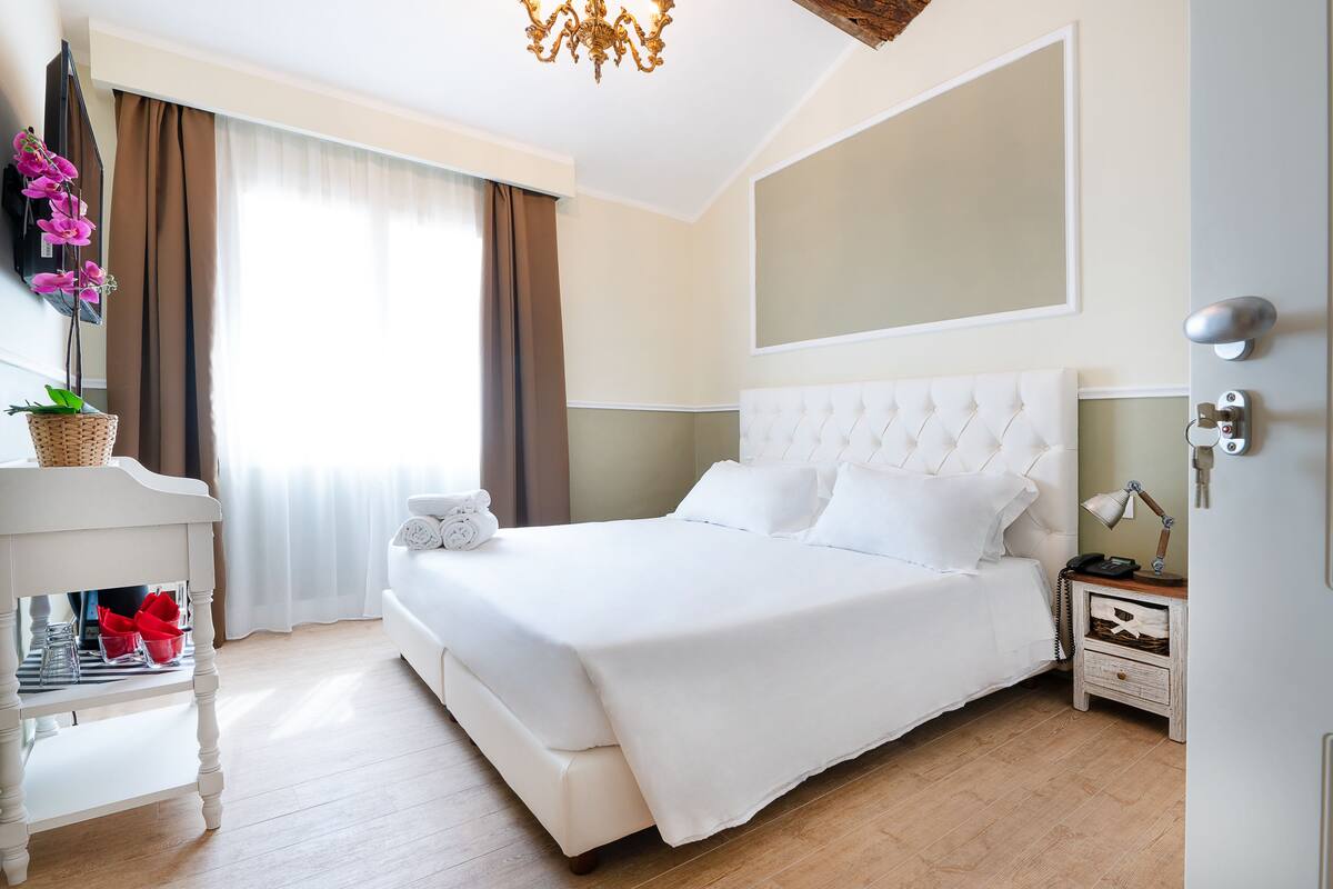 A neatly arranged bedroom with a large bed, a bedside table with a lamp, and a wall-mounted TV.