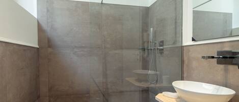 A modern bathroom with a glass-enclosed shower, a large white vessel sink, and a mirror above the sink.
