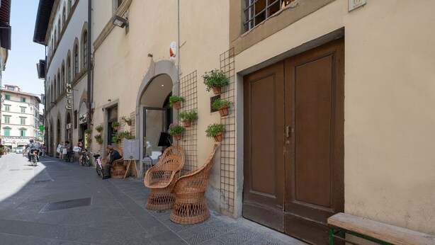 A street with wicker chairs and a bench outside a building with a closed door and a sign that reads "MUSIC". - Residenza d'Epoca la Basilica by Mamo Florence (Florence)