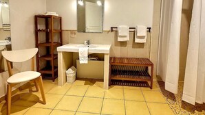Un baño con lavamanos, espejo, silla de madera, estante y cortina de ducha.