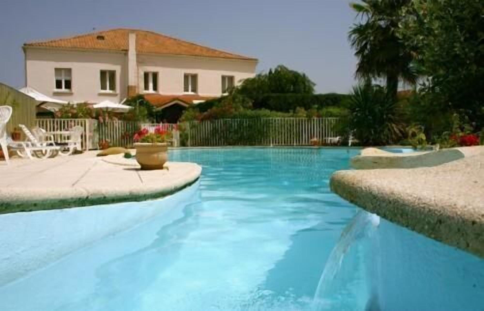 A swimming pool with a clear blue water, surrounded by a white fence, and a building with a tiled roof in the background.