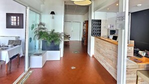 Ein modernes Interieur mit einer Rezeption, einem Essbereich mit weißem Tisch und einem Flur, der in einen weiteren Raum führt.