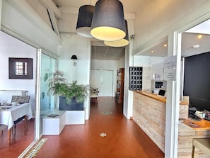 Een modern interieur met een receptiebalie, een eetgedeelte met een witte tafel en een gang die naar een andere kamer leidt.