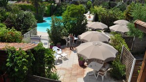 Un patio al aire libre con piscina, rodeado de exuberante vegetación y amueblado con asientos y sombrillas.