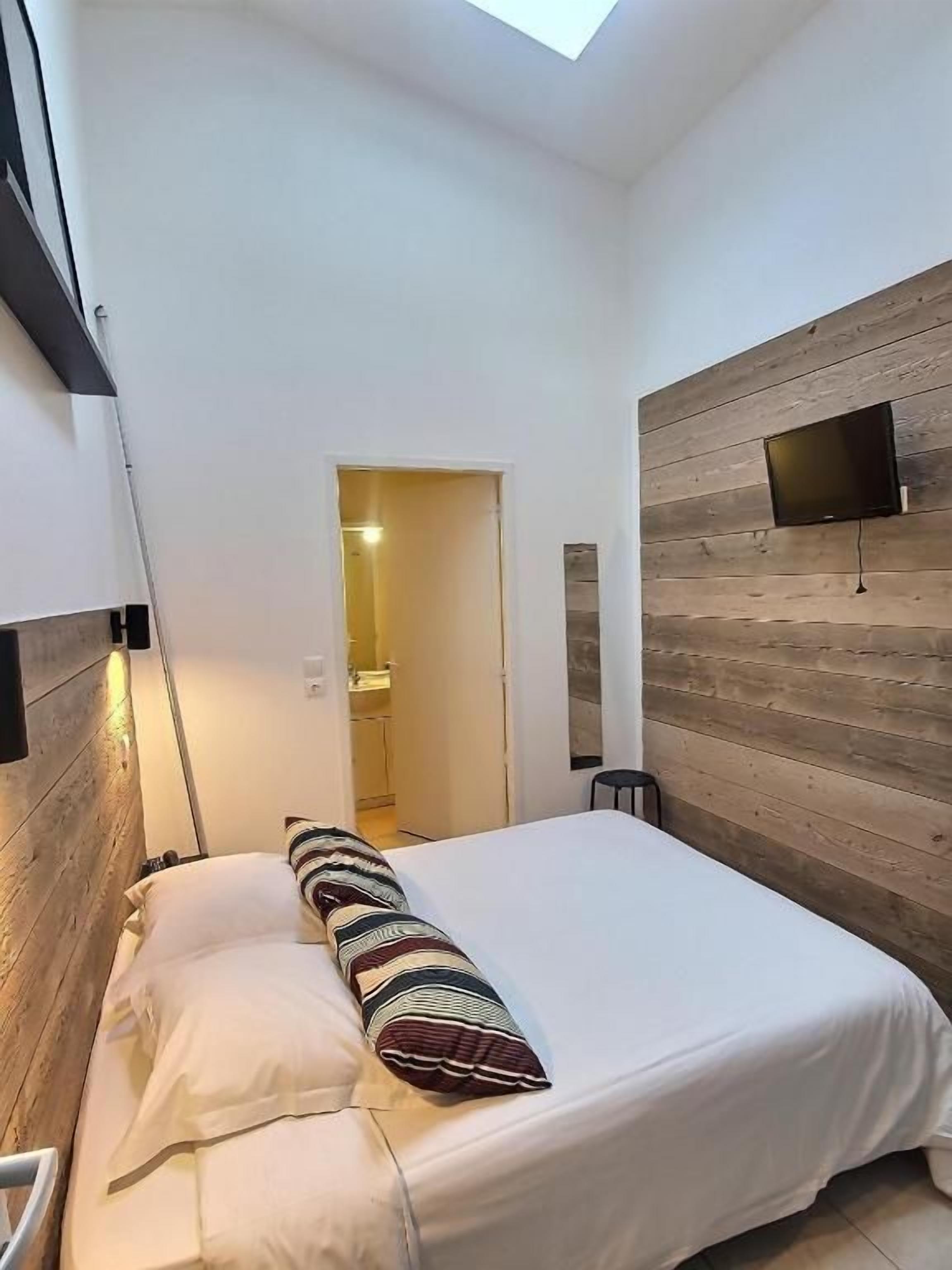 A bedroom with a bed, a wooden wall panel, a flat-screen TV, and a skylight.