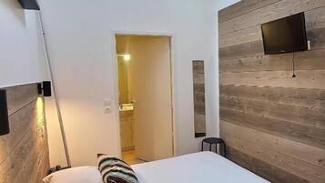 A bedroom with a bed, a wooden wall panel, a flat-screen TV, and a skylight.