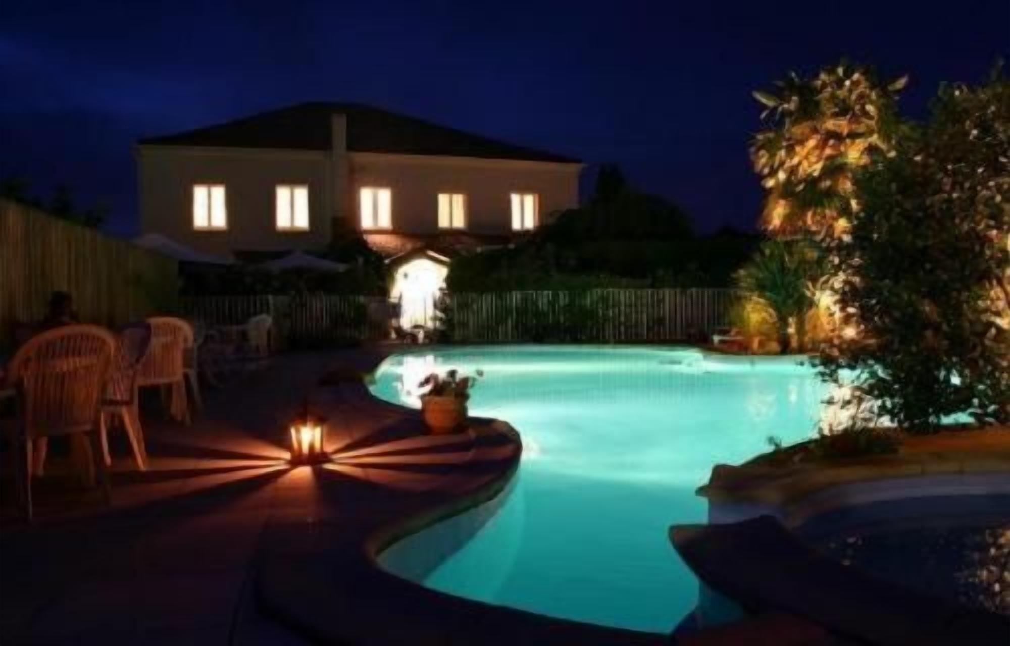 Une piscine la nuit, avec une maison en arrière-plan.