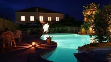Une piscine la nuit, avec une maison en arrière-plan.