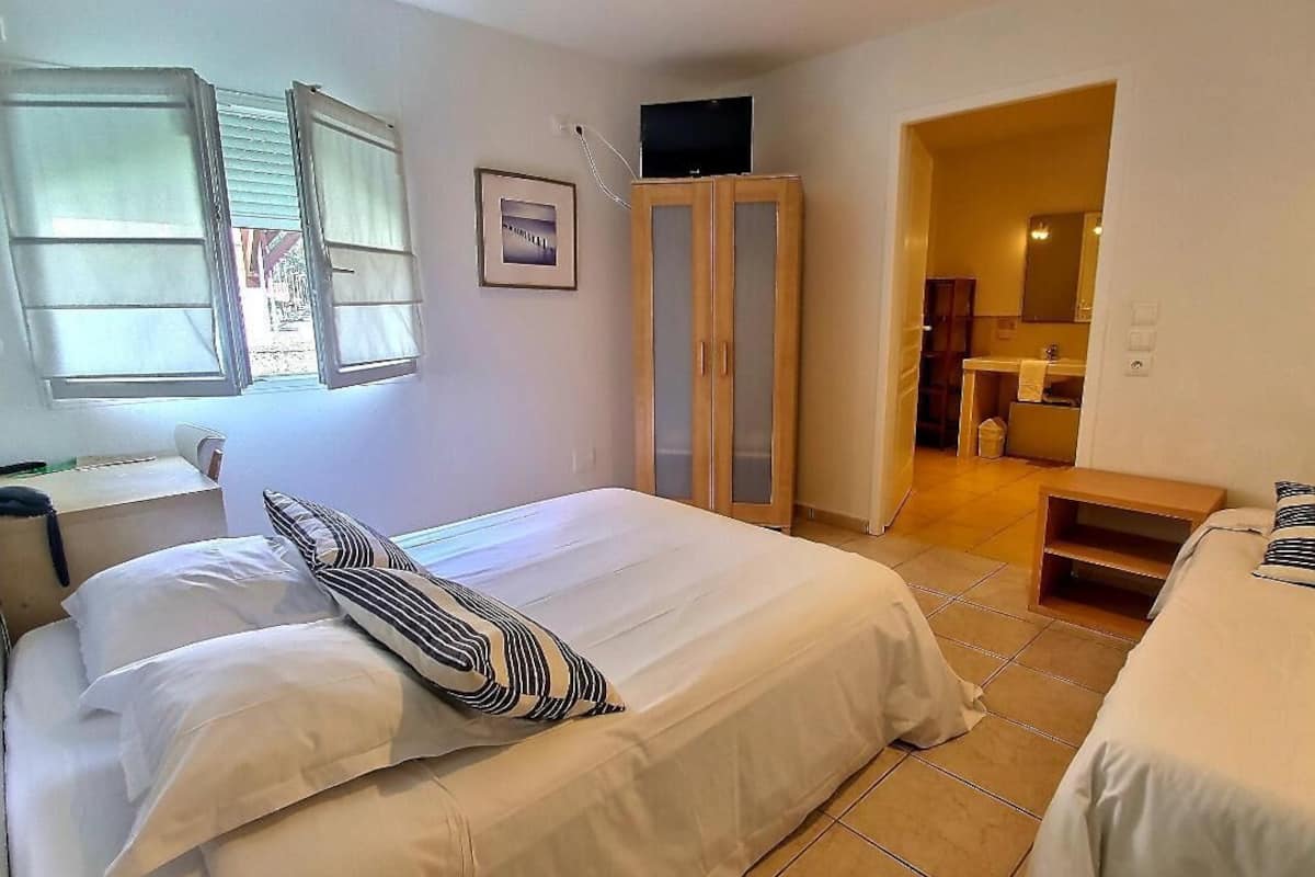 A bedroom with two beds, a wardrobe, a television, and a bathroom visible through an open door.
