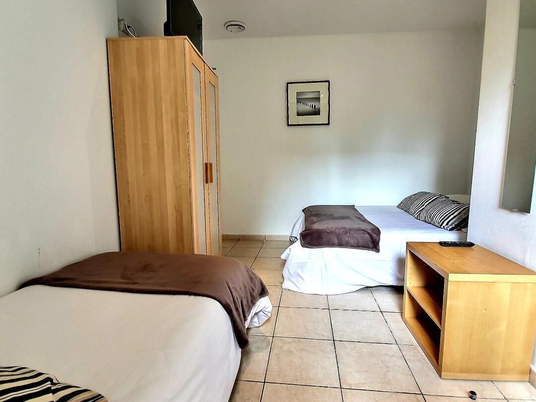 A bedroom with two beds, a wooden wardrobe, a small wooden table, and a framed picture on the wall.