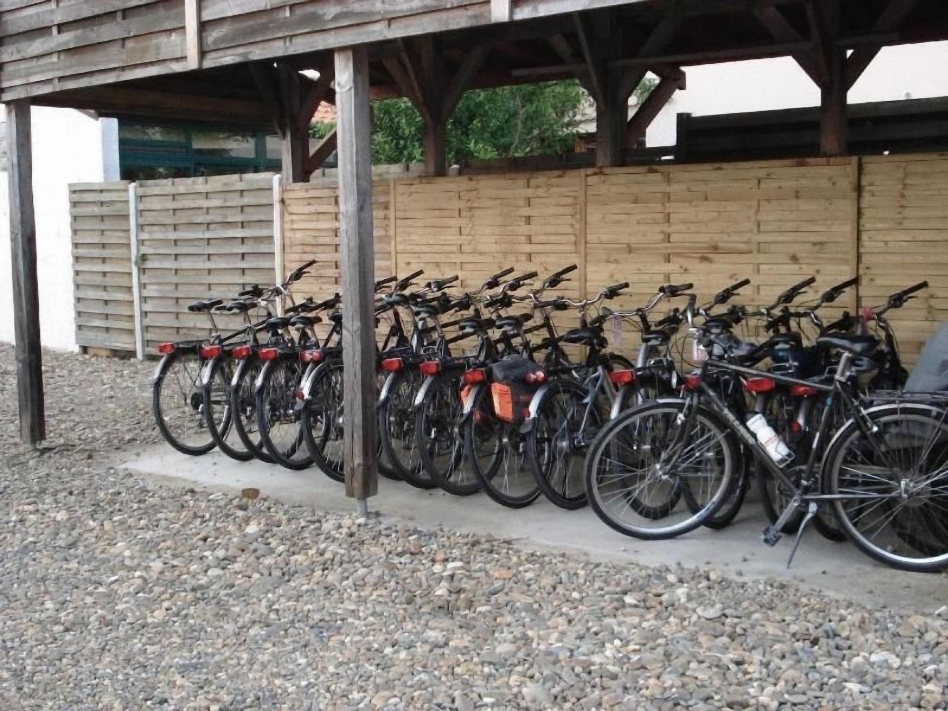 A row of bicycles parked under a wooden shelter with a gravel ground.