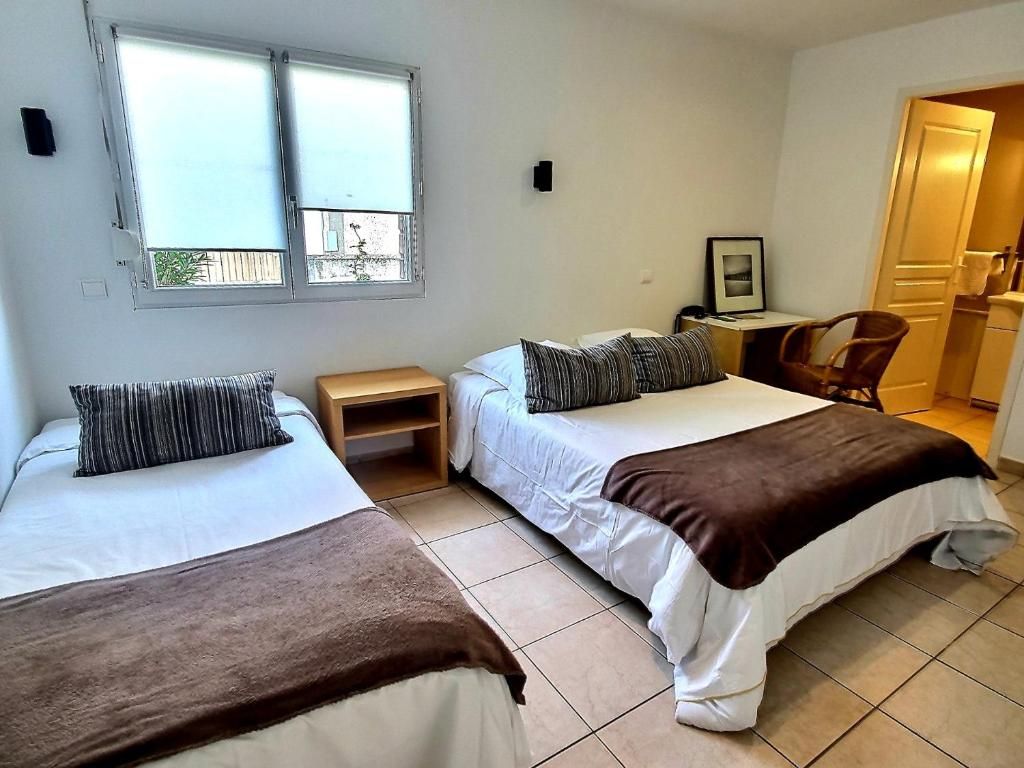 Ein Schlafzimmer mit zwei Betten, einem kleinen Tisch, einem Stuhl und einem Fenster.