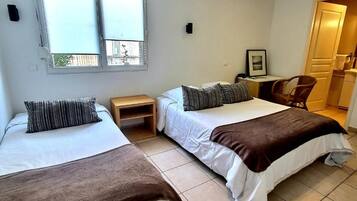 A bedroom with two beds, a small table, a chair, and a window.